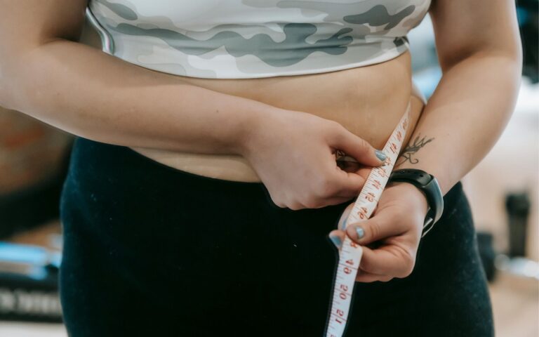 Mulher em roupa de academia medindo a cintura com fita métrica, simbolizando a jornada de emagrecimento consciente e a busca por qualidade de vida.
